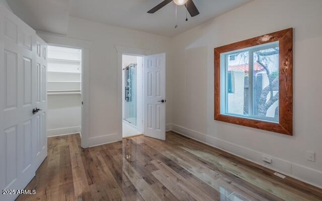 unfurnished bedroom with a walk in closet, baseboards, wood finished floors, and ceiling fan