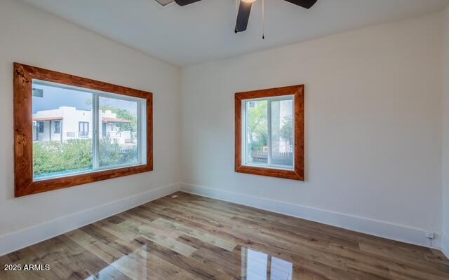 empty room featuring wood finished floors, baseboards, and ceiling fan