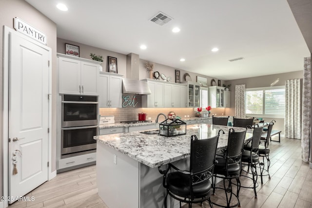 kitchen featuring wall chimney exhaust hood, a kitchen bar, sink, stainless steel appliances, and a kitchen island with sink