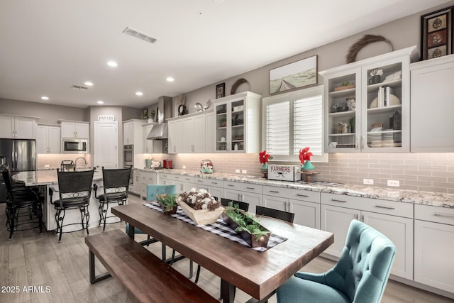 kitchen with white cabinetry, appliances with stainless steel finishes, light stone counters, and light hardwood / wood-style flooring