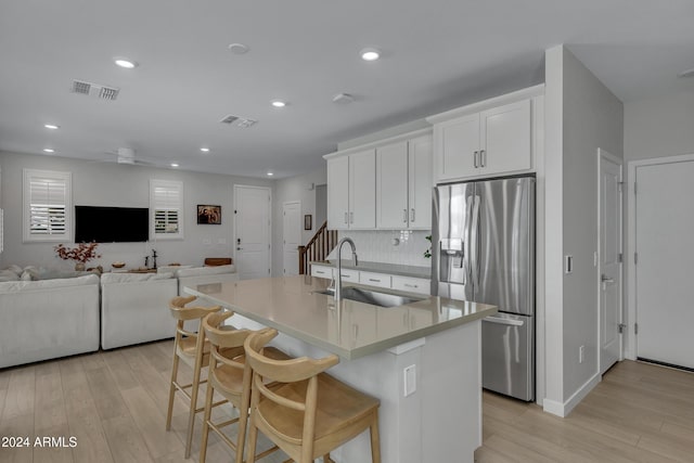 kitchen with white cabinetry, sink, a breakfast bar area, stainless steel refrigerator with ice dispenser, and a center island with sink