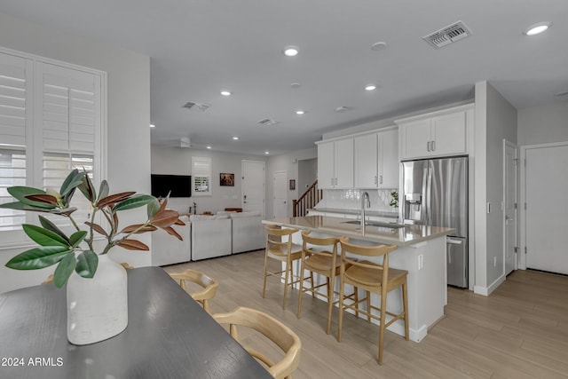 kitchen featuring sink, white cabinetry, stainless steel refrigerator with ice dispenser, a kitchen bar, and light wood-type flooring