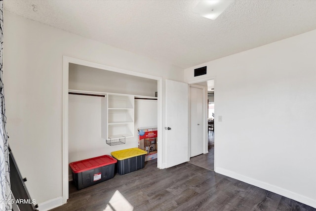 unfurnished bedroom featuring a textured ceiling, a closet, dark wood finished floors, and baseboards