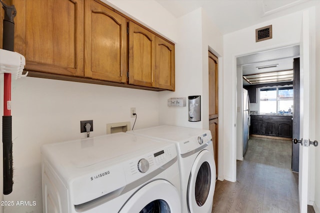 laundry area featuring visible vents, cabinet space, washer and clothes dryer, and wood finished floors