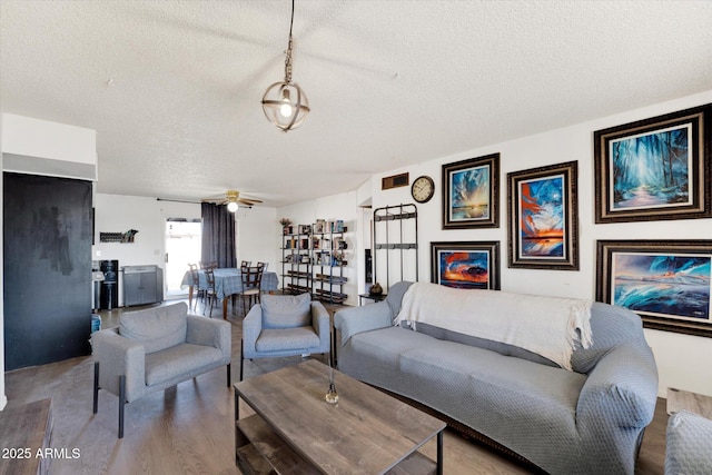 living room featuring a ceiling fan, a textured ceiling, and wood finished floors