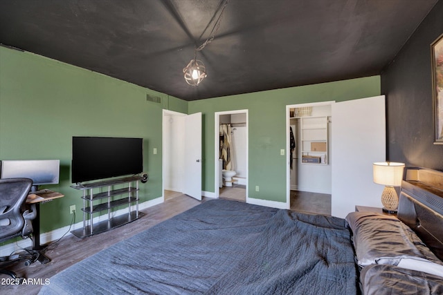 bedroom with ensuite bath, baseboards, visible vents, and wood finished floors