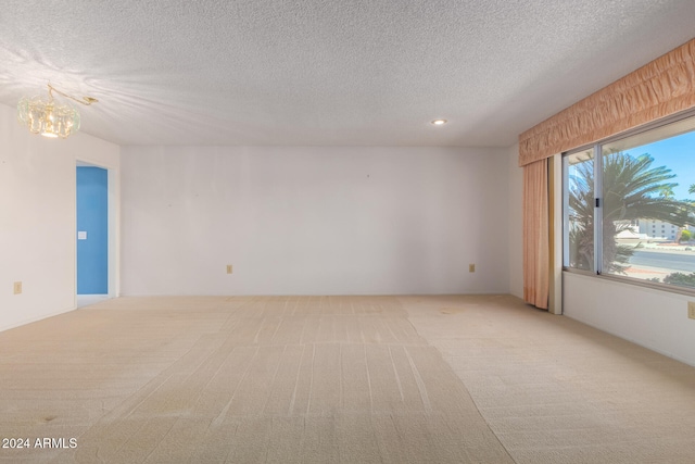 empty room featuring a textured ceiling, a notable chandelier, and light carpet