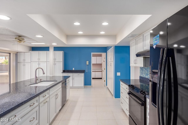 kitchen featuring a tray ceiling, sink, black appliances, dark stone countertops, and white cabinets