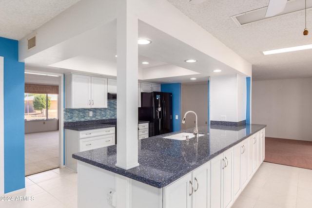 kitchen with black fridge, dark stone counters, sink, light tile patterned floors, and white cabinetry