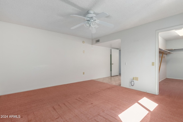 unfurnished bedroom with a walk in closet, ceiling fan, a textured ceiling, light colored carpet, and a closet