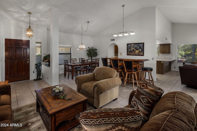 tiled living room with high vaulted ceiling, an inviting chandelier, and a textured ceiling