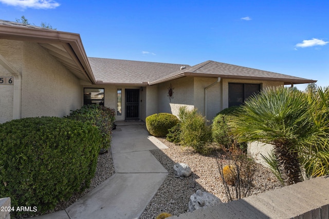 view of exterior entry with roof with shingles and stucco siding