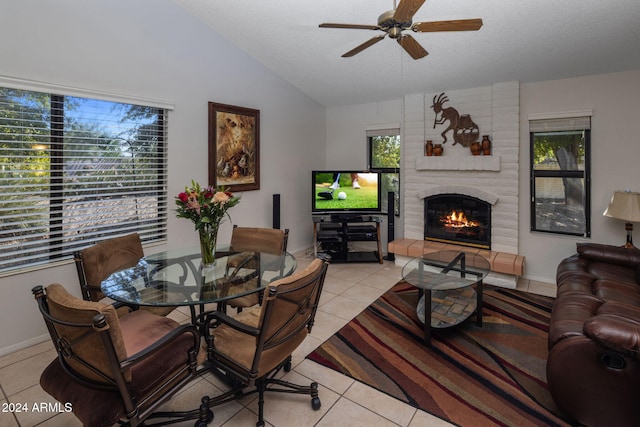 living room with ceiling fan, light tile patterned floors, a textured ceiling, a fireplace, and vaulted ceiling