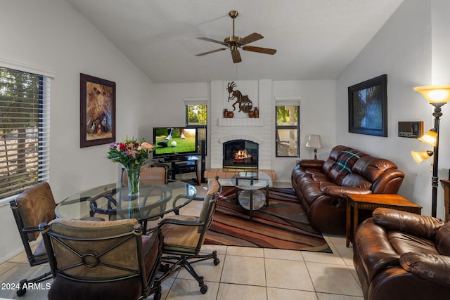 living area with light tile patterned floors, ceiling fan, a brick fireplace, and lofted ceiling