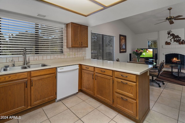 kitchen featuring a brick fireplace, sink, light tile patterned flooring, kitchen peninsula, and dishwasher