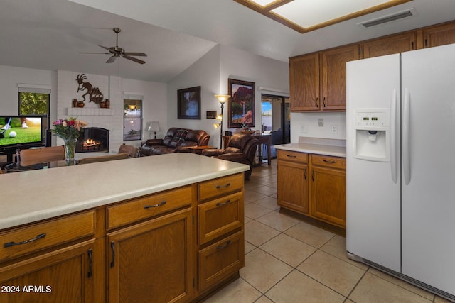 kitchen with ceiling fan, light tile patterned floors, a brick fireplace, white fridge with ice dispenser, and vaulted ceiling