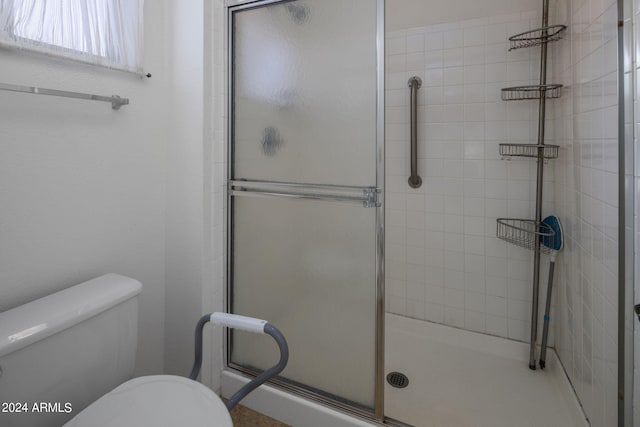 bathroom featuring a shower with door and toilet