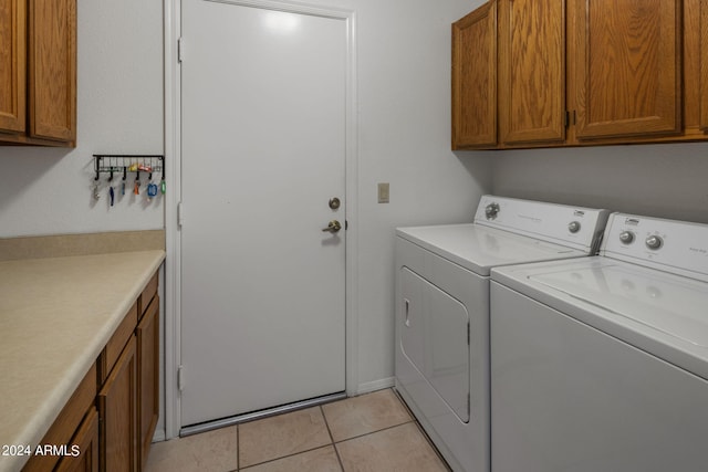 clothes washing area with washing machine and dryer, light tile patterned floors, and cabinets