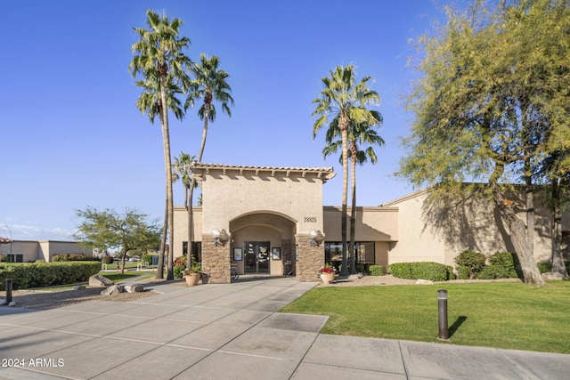 mediterranean / spanish-style house featuring driveway, stucco siding, stone siding, and a front yard
