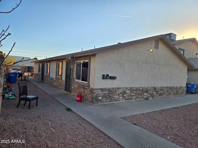 property exterior at dusk with stone siding, fence, cooling unit, and stucco siding