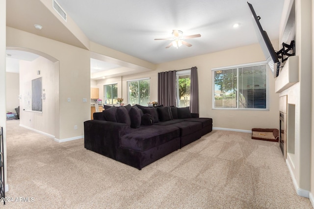 living room featuring light carpet, baseboards, a ceiling fan, a fireplace, and arched walkways