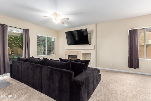living area featuring light colored carpet, ceiling fan, a fireplace, and baseboards