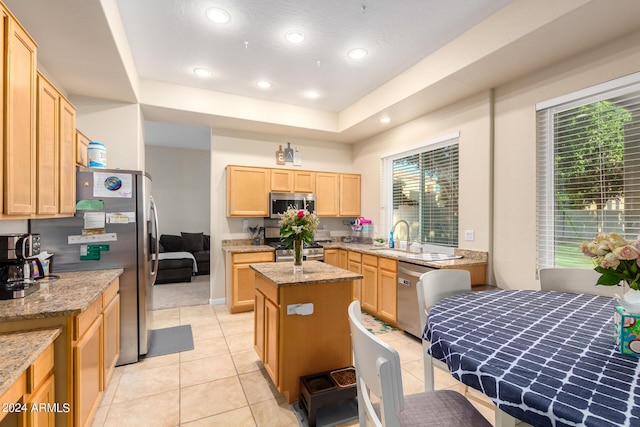 kitchen with appliances with stainless steel finishes, light brown cabinetry, light stone counters, a center island, and a sink