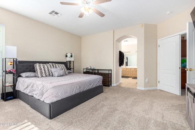 bedroom with light carpet, arched walkways, a ceiling fan, connected bathroom, and baseboards