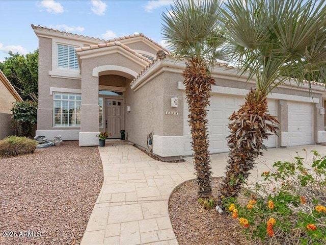 mediterranean / spanish house with stucco siding, an attached garage, and a tiled roof