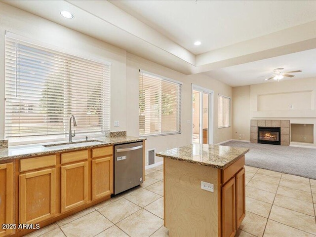 kitchen with dishwasher, a sink, light tile patterned flooring, a ceiling fan, and light stone counters