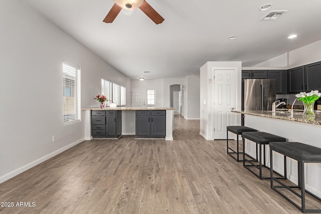 kitchen with light stone counters, arched walkways, freestanding refrigerator, a ceiling fan, and visible vents