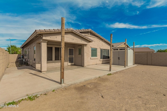rear view of house with a fenced backyard, stucco siding, a patio area, a tiled roof, and a storage shed