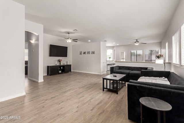 living room with baseboards, a ceiling fan, arched walkways, and light wood-style flooring