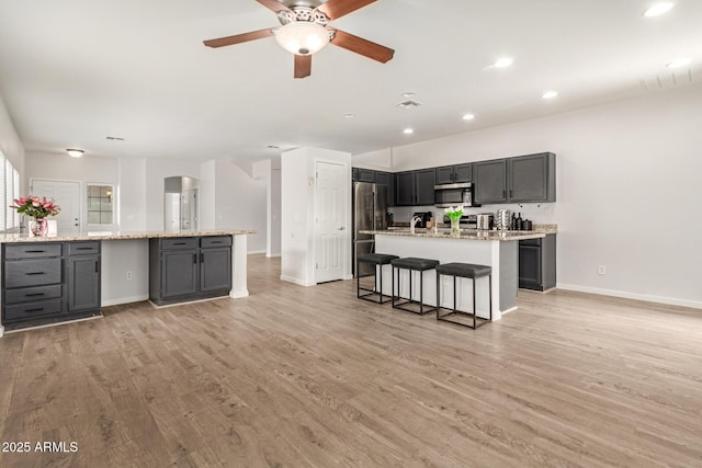 kitchen featuring baseboards, appliances with stainless steel finishes, an island with sink, and light wood-type flooring