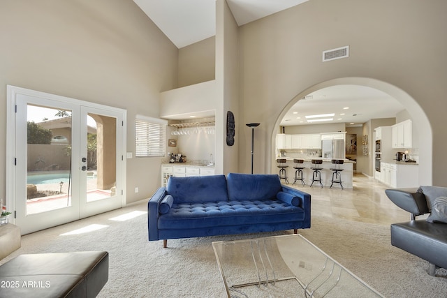 carpeted living room with french doors, high vaulted ceiling, and wet bar