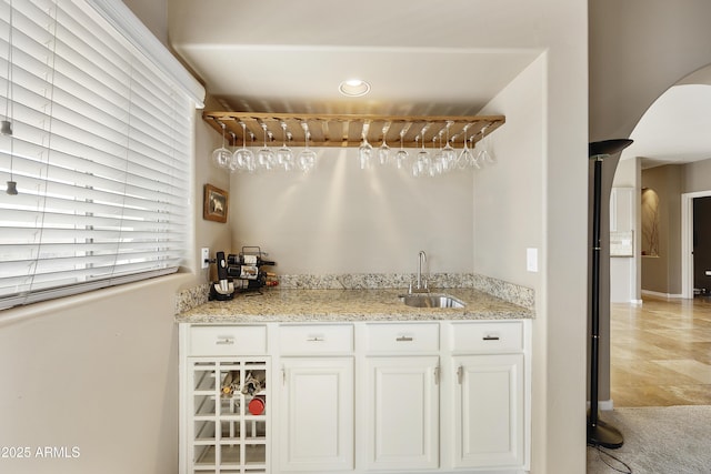 bar with white cabinets, light stone counters, and sink