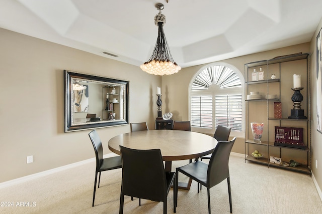 carpeted dining area with a chandelier and a tray ceiling