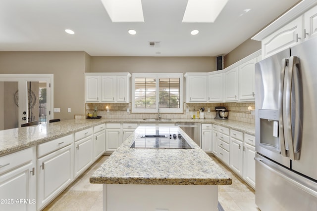 kitchen with appliances with stainless steel finishes, a skylight, tasteful backsplash, sink, and white cabinetry