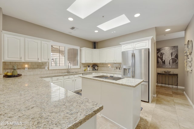 kitchen featuring a center island, white cabinets, black electric stovetop, a skylight, and light stone countertops