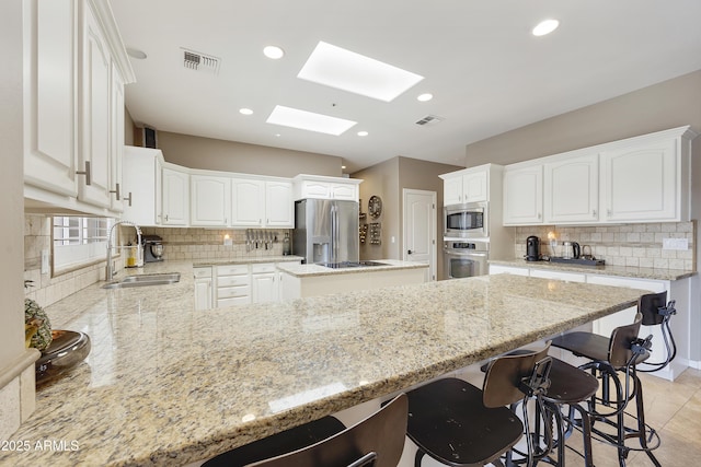 kitchen with tasteful backsplash, a skylight, stainless steel appliances, sink, and white cabinetry