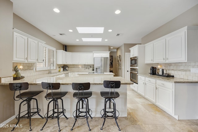 kitchen with white cabinets, a kitchen breakfast bar, stainless steel appliances, and a skylight