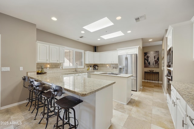 kitchen featuring appliances with stainless steel finishes, a skylight, light stone counters, white cabinets, and a breakfast bar area