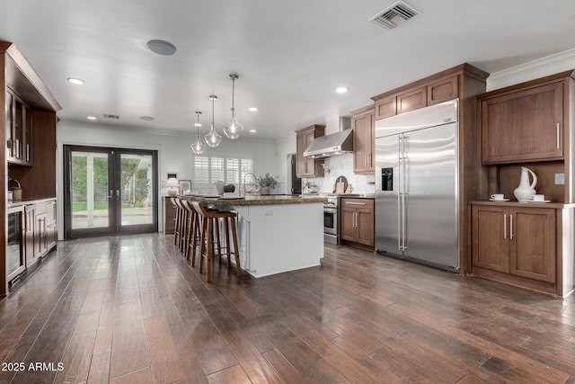 kitchen featuring high end appliances, wall chimney range hood, pendant lighting, a kitchen island, and a breakfast bar area