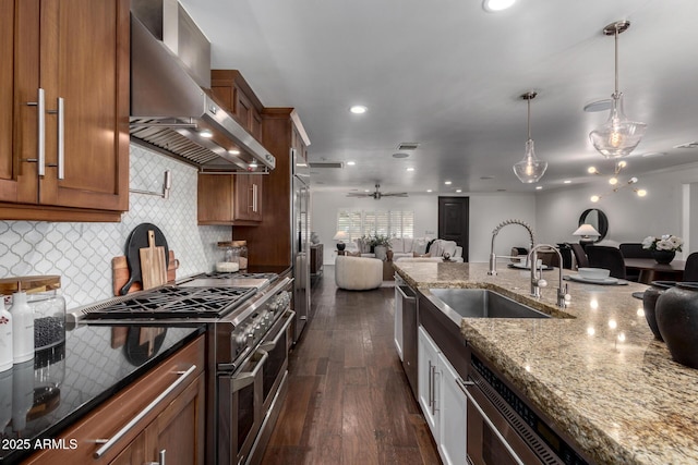 kitchen with pendant lighting, high end appliances, wall chimney range hood, sink, and dark stone countertops