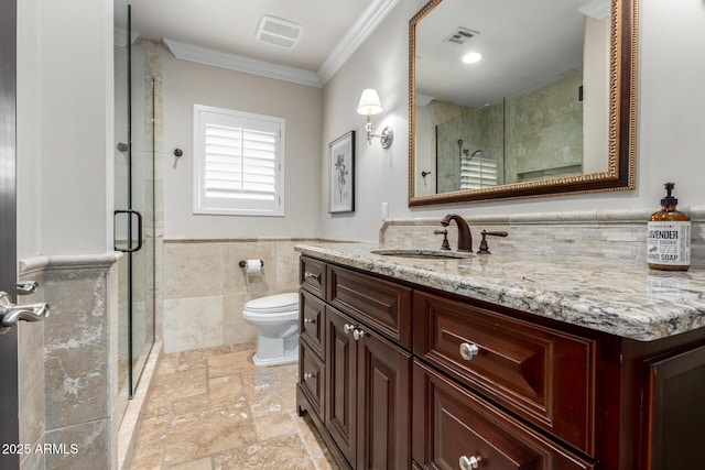 bathroom featuring vanity, toilet, ornamental molding, tile walls, and a shower with shower door