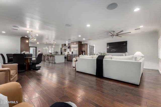 living room with ceiling fan with notable chandelier, dark hardwood / wood-style flooring, and ornamental molding