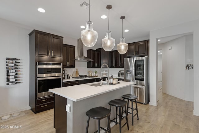 kitchen featuring visible vents, wall chimney range hood, light countertops, appliances with stainless steel finishes, and light wood-style floors