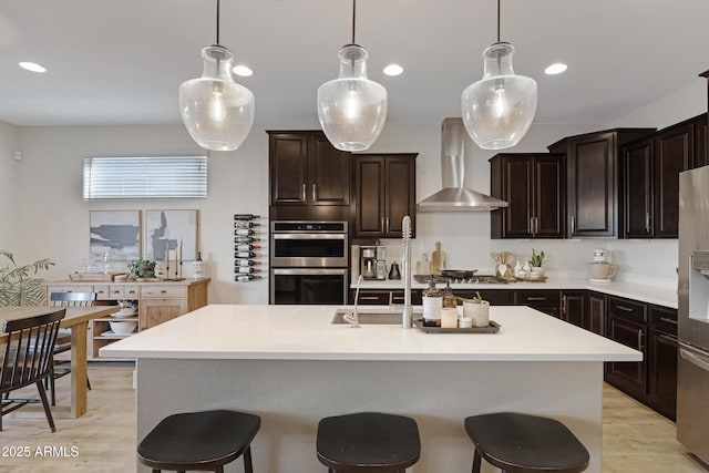 kitchen featuring a kitchen breakfast bar, wall chimney range hood, light countertops, and stainless steel appliances