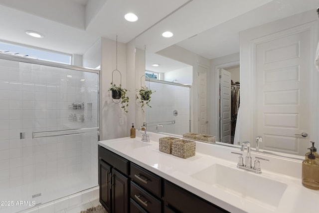 bathroom featuring a walk in closet, a shower stall, double vanity, and a sink