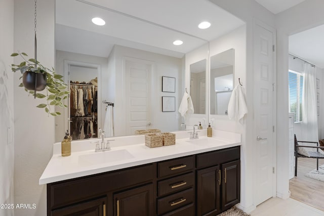 full bath with a walk in closet, double vanity, recessed lighting, and a sink